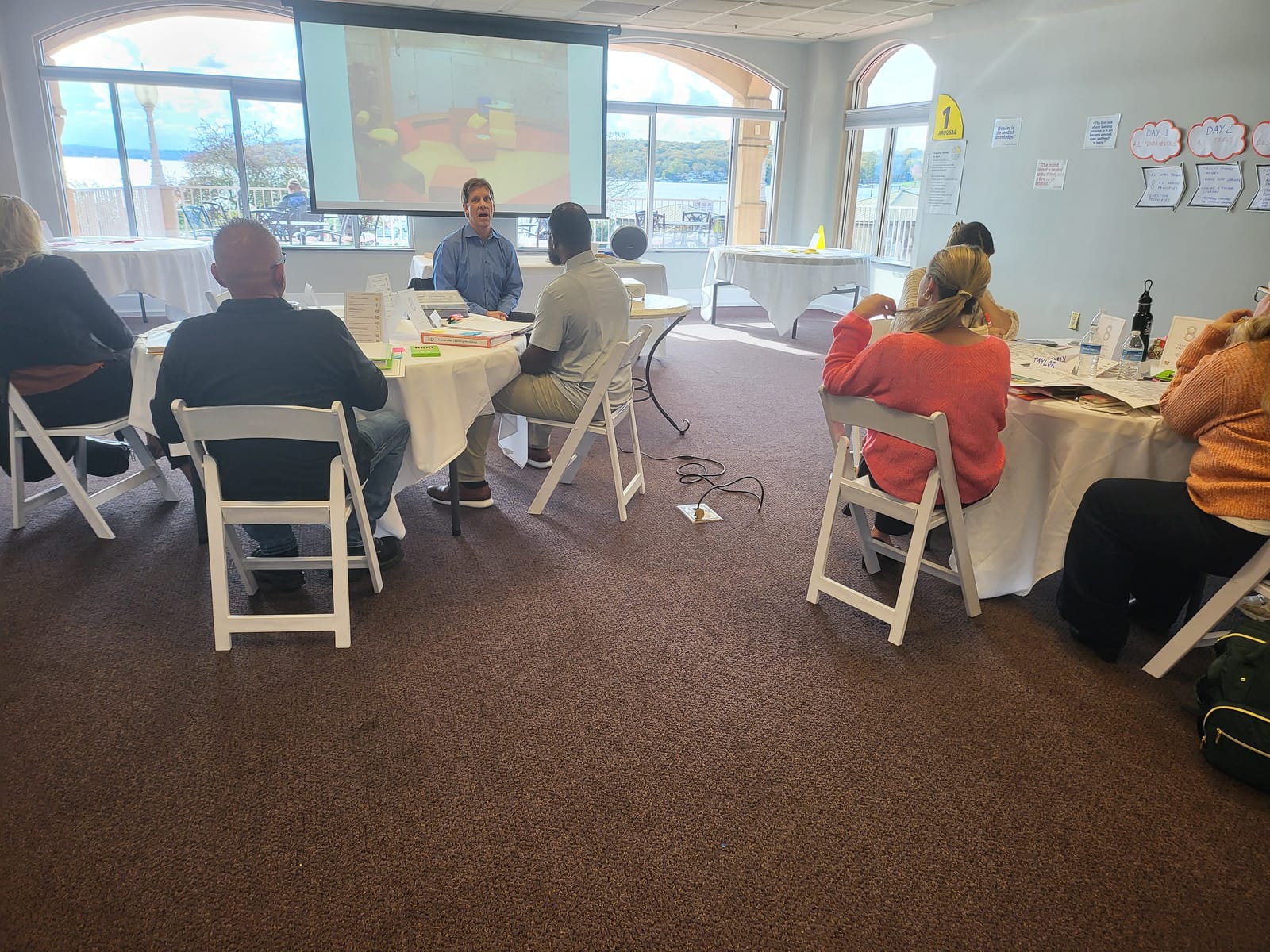 Workshop participants at round tables in a bright room with windows onto Geneva Lake