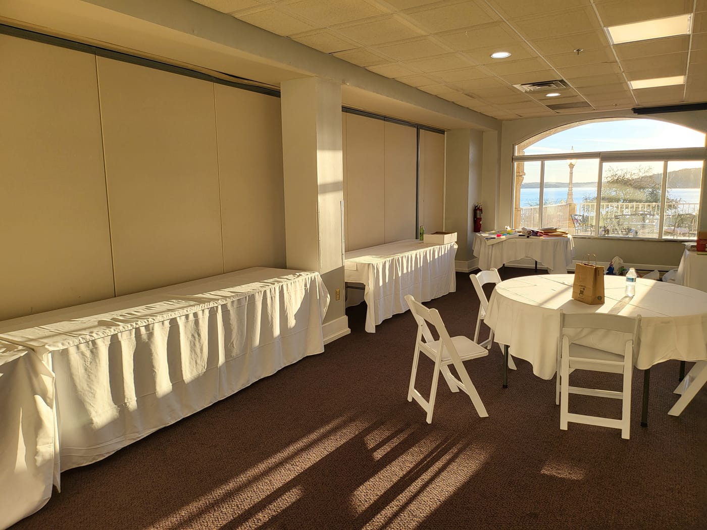 Round tables with white linens set for a workshop, lake light through tall windows